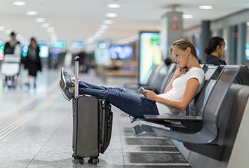 Kvinna sitter på en bänk på en flygplats med fötterna på en resväska