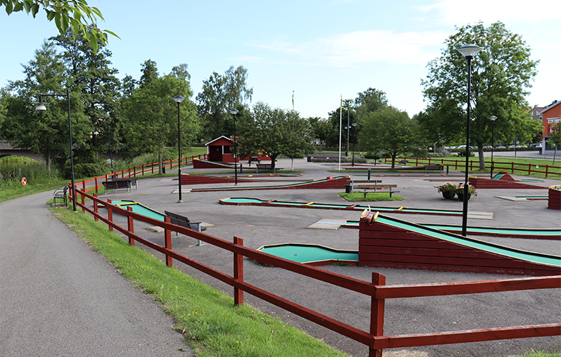 Minigolfbanor i en grönskande miljö, intill en cykelväg och vatten.