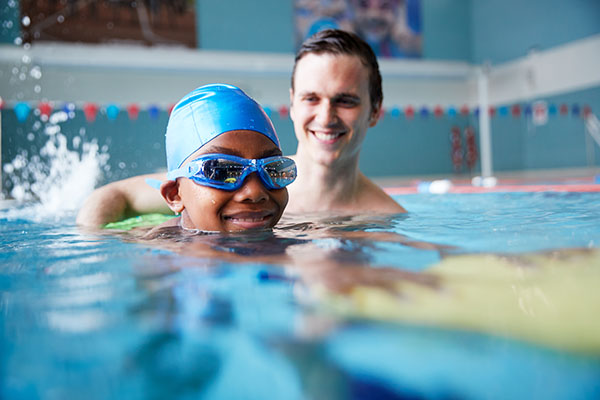En pojke får hjälp av en simlärare att lära sig simma.