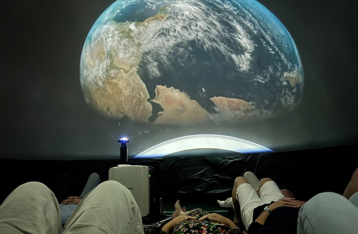 Personer som ligger ner och tittar på en stor jordglob på en skärm.