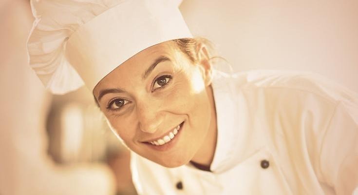 En leende kvinna i kockmössa och kockrock.