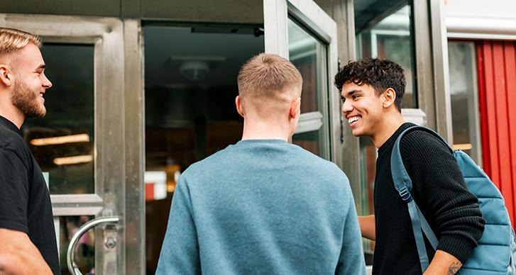 Tre elever står vi entrén till skolan, på väg in i skolan. 