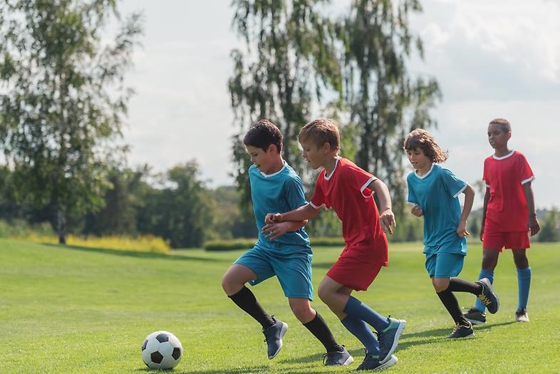 Barn spelar fotboll på en grön gräsmatta