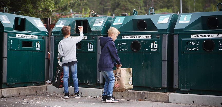 Barn som slänger förpackningar på en återvinningsstation.