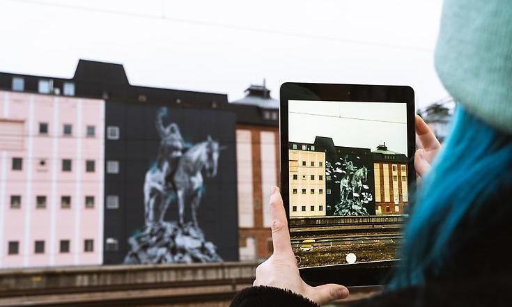 En person håller i en mobiltelefon riktat mot fasadmålning vid stationen i Mjölby. Foto: Fredrik Åkerberg