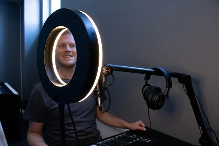 En podstudio med hörlurar och kontroller för ljud. En person syns genom en ringlampa.