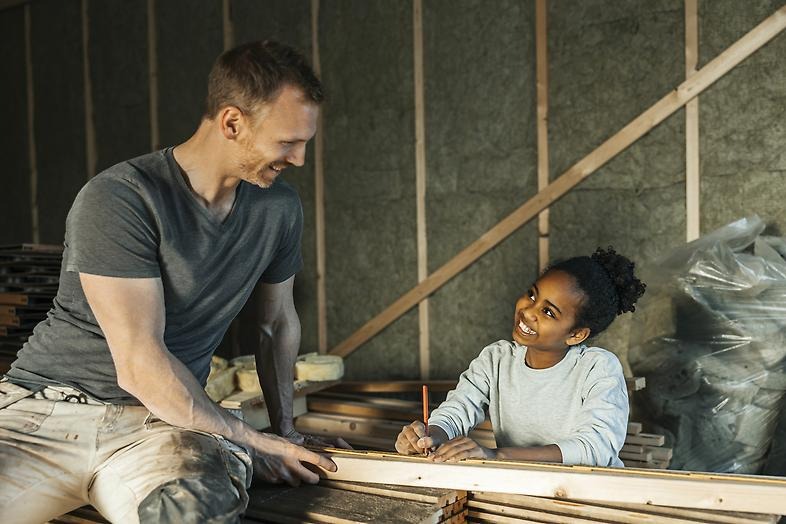 En man som sitter på en hög med brädor och ett barn som mäter på brädan.