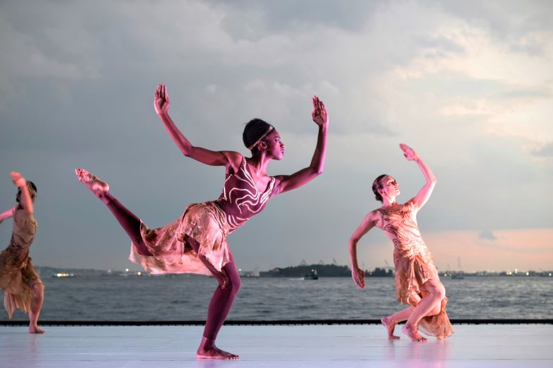 Tre kvinnor i dansrörelser på en scen i bakgrunden är en vattenspegel