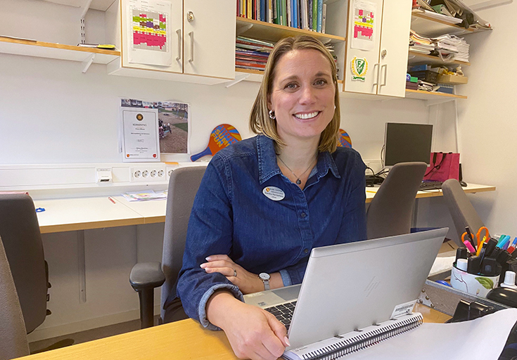 Sandra Hennerberg sitter i ett personalrum med datorn framför sig.