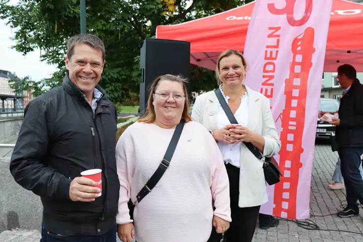 Tre leende personer med Mjölby station och flaggor med texten "Östgötapendeln" i bakgrunden.