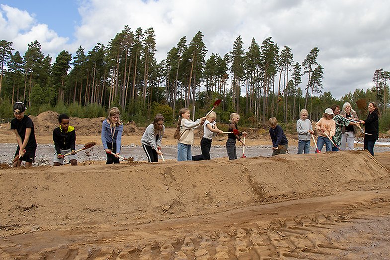 Tio barn gräver i en sandhög. 