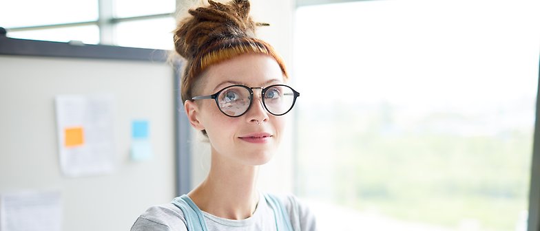 Porträttbild på en kvinna med glasögon och dreads som befinner sig i en skolmiljö. 