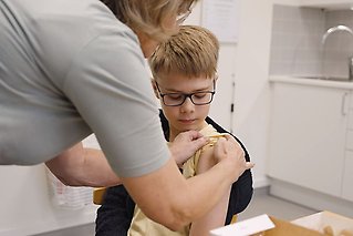 Skolsköterska drar upp ärmen inför vaccination på en elev. 