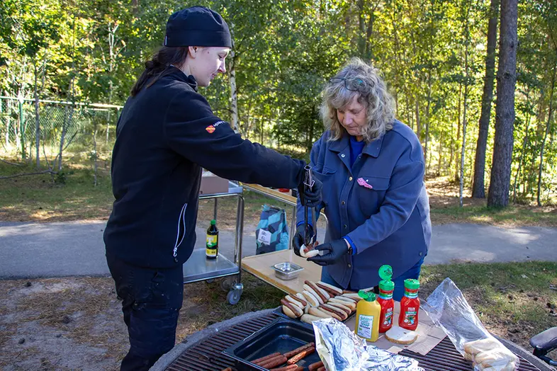 Två personer står vid en grill där de grillar korv.