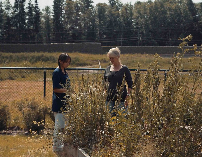 En yngre medarbetare står i en trädgård med en boende på en gruppbostad inom LSS.