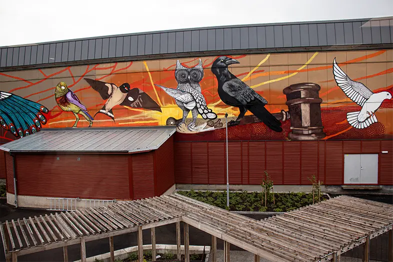 Fasaden av en byggnad med stor målning som föreställer fem olika fåglar och en domarklubba.