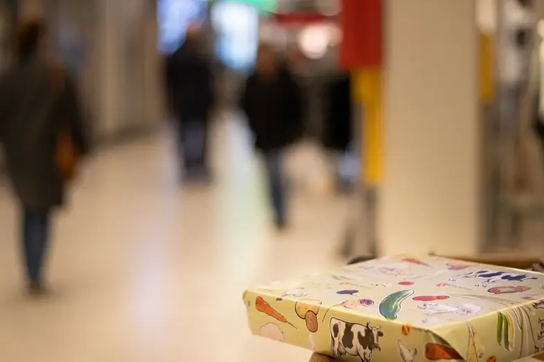 Ett paket inslaget i Mjölby-kommun-papper i Galleria Kvarnen. Ett myller av människor går mellan butikerna.