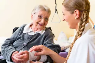 En äldre kvinna som får hjälp med sitt bandage på armen av en kvinna med lång fläta.