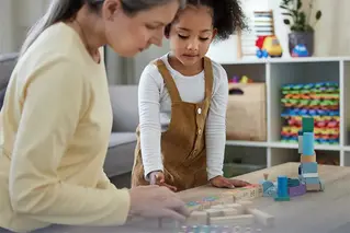 Förskolepedagog och ett barn pysslar vid ett bord