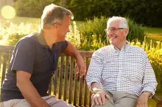 Två män sittande på en parkbänk, som ler mot varandra.