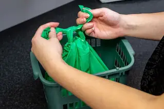 Två händer som knyter ihop gröna påsen