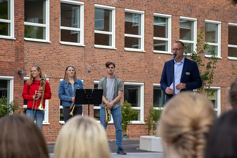 Tre personer med blåsinstrument och Joachim som håller tal. 